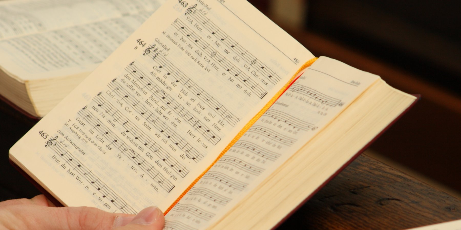 An open hymnal on dark wood, sheet music visible on the page.